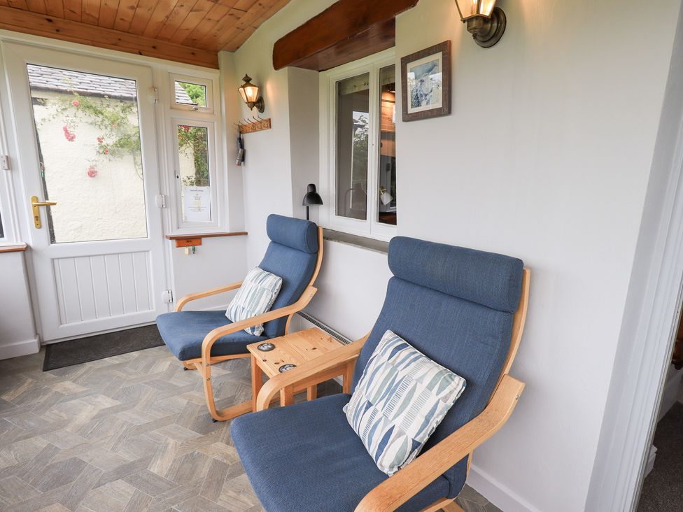 A conservatory with two armchairs and a table at Squirrel Cottage in Bassenthwaite