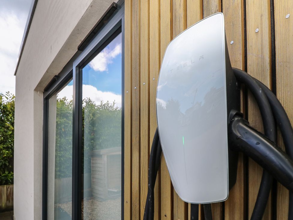 A Tesla charger mounted on a wooden wall next to a glass window at Aquanaut in Gurnard