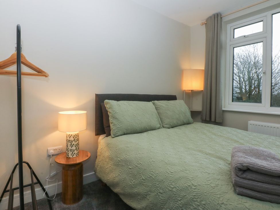 A bedroom with a green bedspread and a lamp on the side table at Caledfryn in Benllech