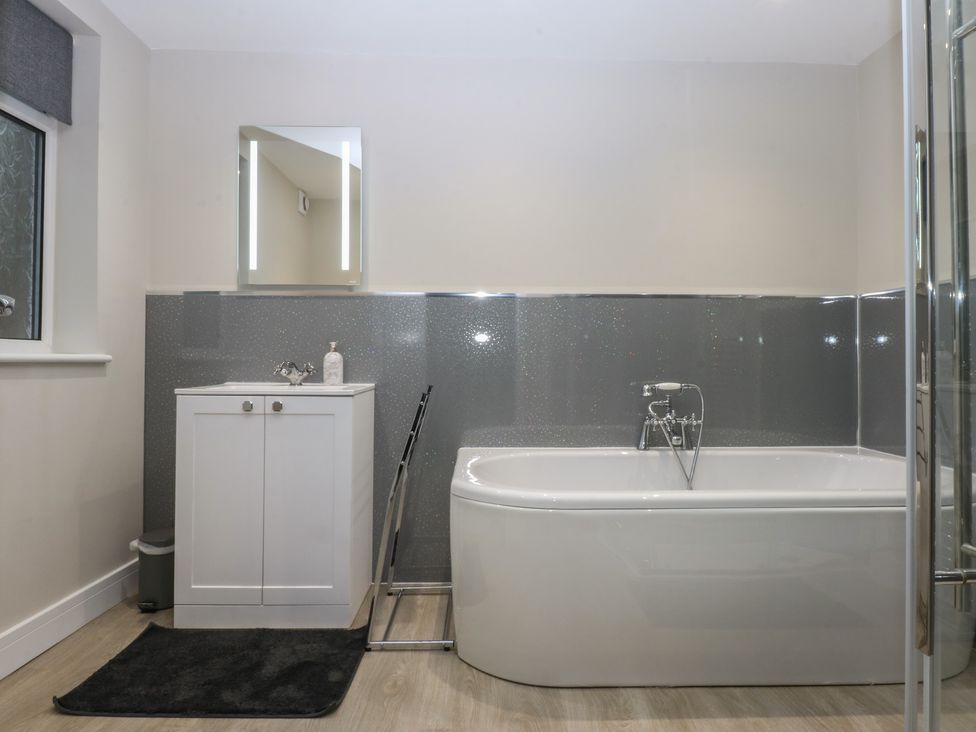 A bathroom with a bathtub, sink, and mirror at Caledfryn in Benllech