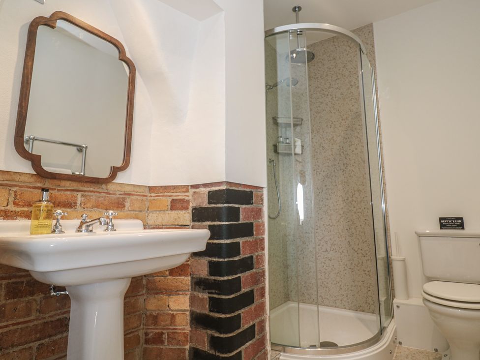 A bathroom with a wash basin, mirror, shower, and toilet at Penmarth House Coverack