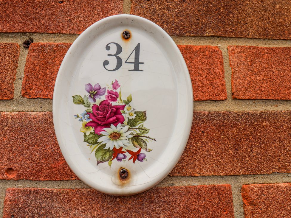 A house number plaque with floral design on a brick wall at 34 Fountain Close Whitby