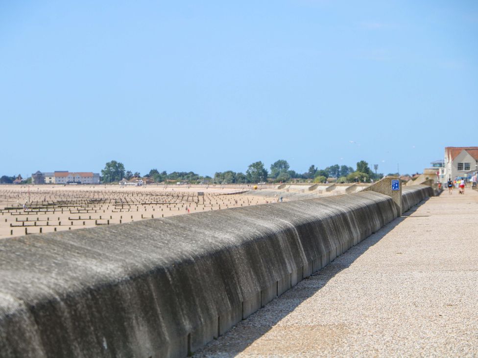 A view of a beach with a sea wall and distant buildings at Dymchurch Bungalow in Romney Marsh