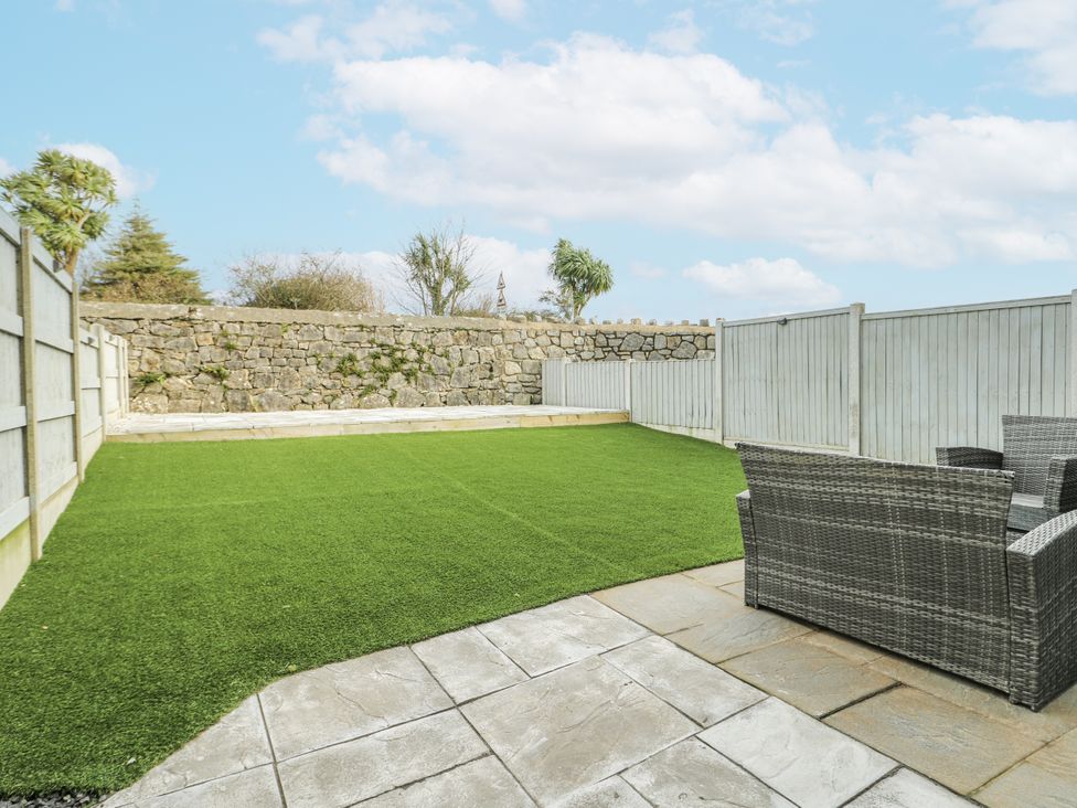 A garden with artificial grass and a stone wall at Y Ty Pren in Brynteg near Benllech