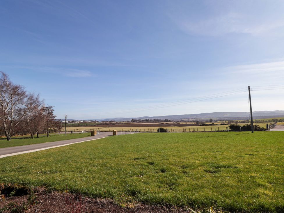 A view of grassland and road with trees and mountains in the background at Nanville in Muir of Ord and Beauly