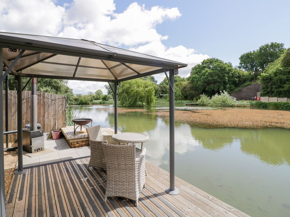 An outdoor area with a gazebo, table, and chairs by a lake at Oak Lodge At Bridge Lake Farm & Fishery Chacombe