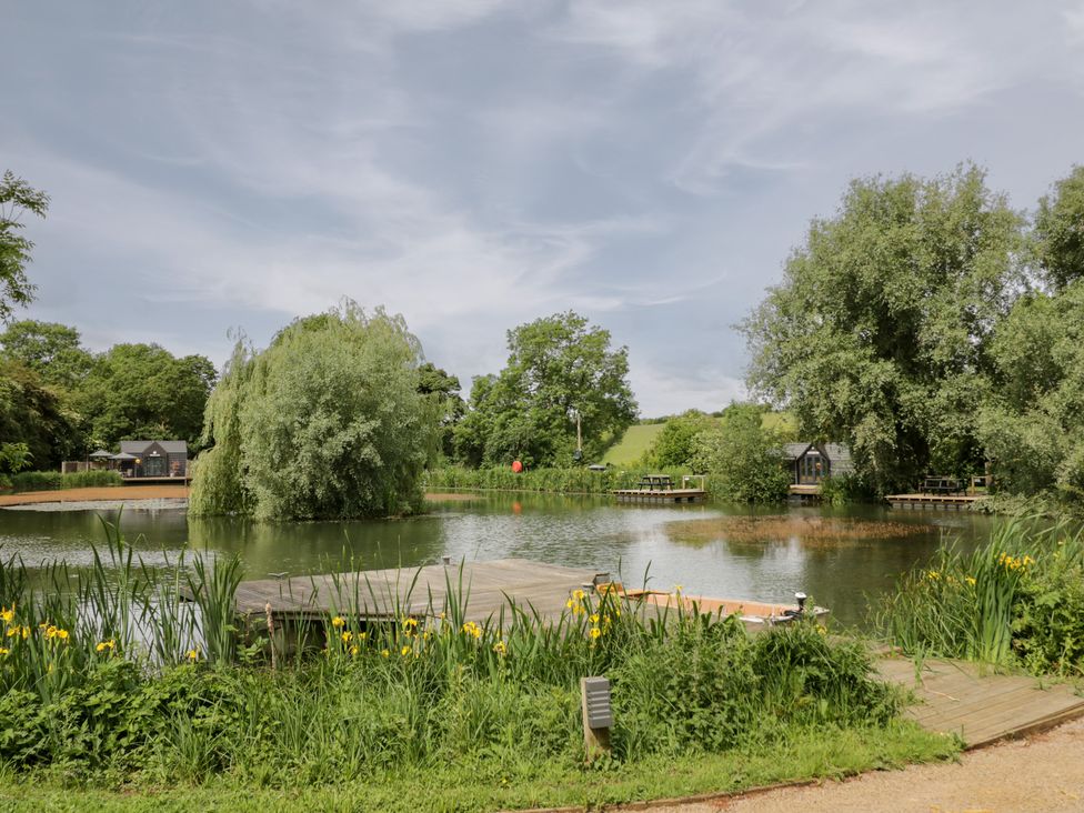 A pond with trees and a dock at Oak Lodge At Bridge Lake Farm & Fishery Chacombe