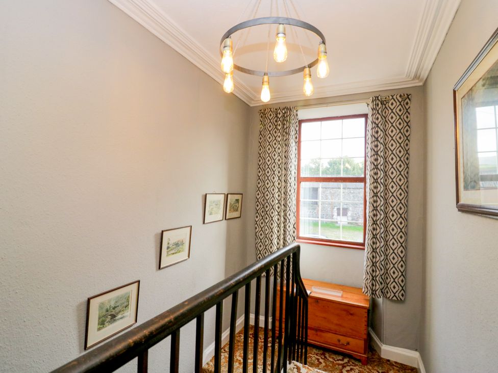 A staircase with a light fixture and framed pictures in a hallway at Beckside Farm in Bootle near Millom, Cumbria