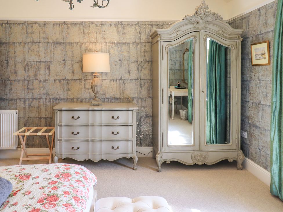 A bedroom with a lamp, wardrobe, and chest of drawers at Fern Bank in Penrith
