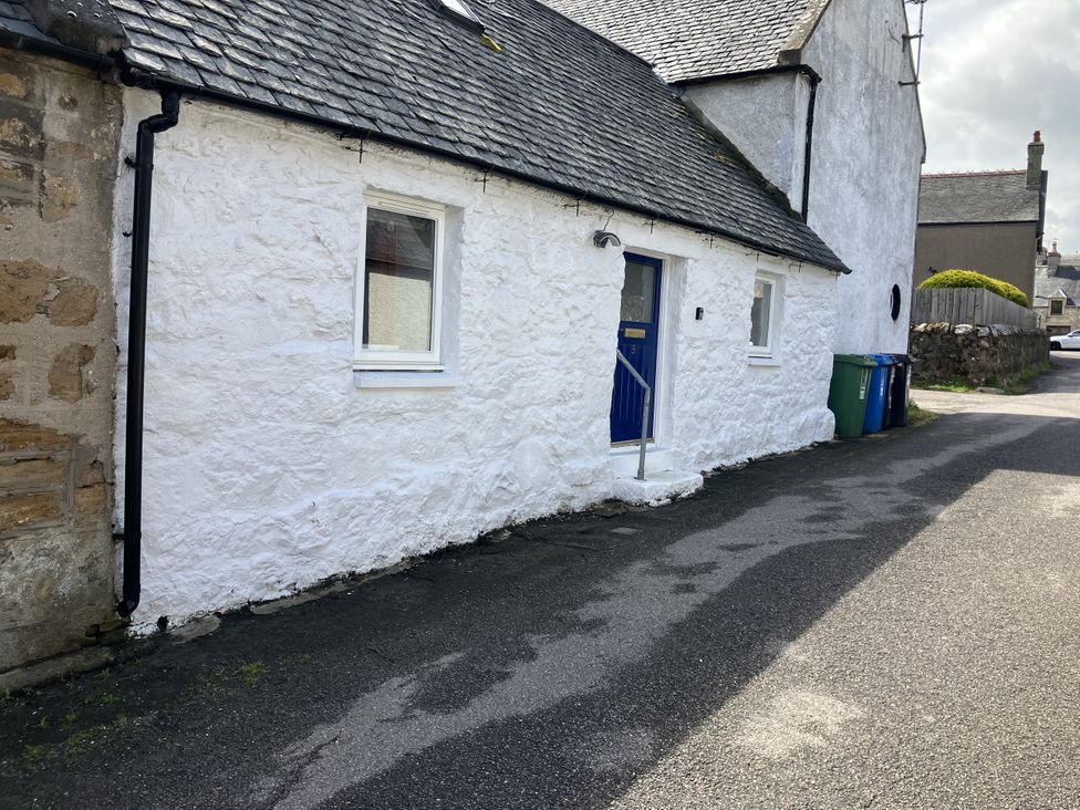 An outdoor view of a cottage with a blue door and a window at 3 Dunrobin Street Tain