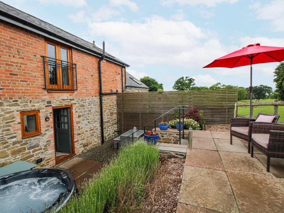 An outdoor space with a hot tub and seating at Meadow Barn in Aston On Clun