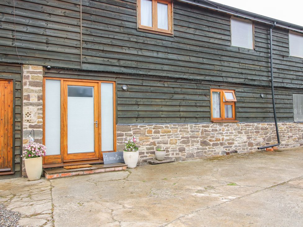 An entrance with a wooden door and stone wall at Meadow Barn in Aston On Clun