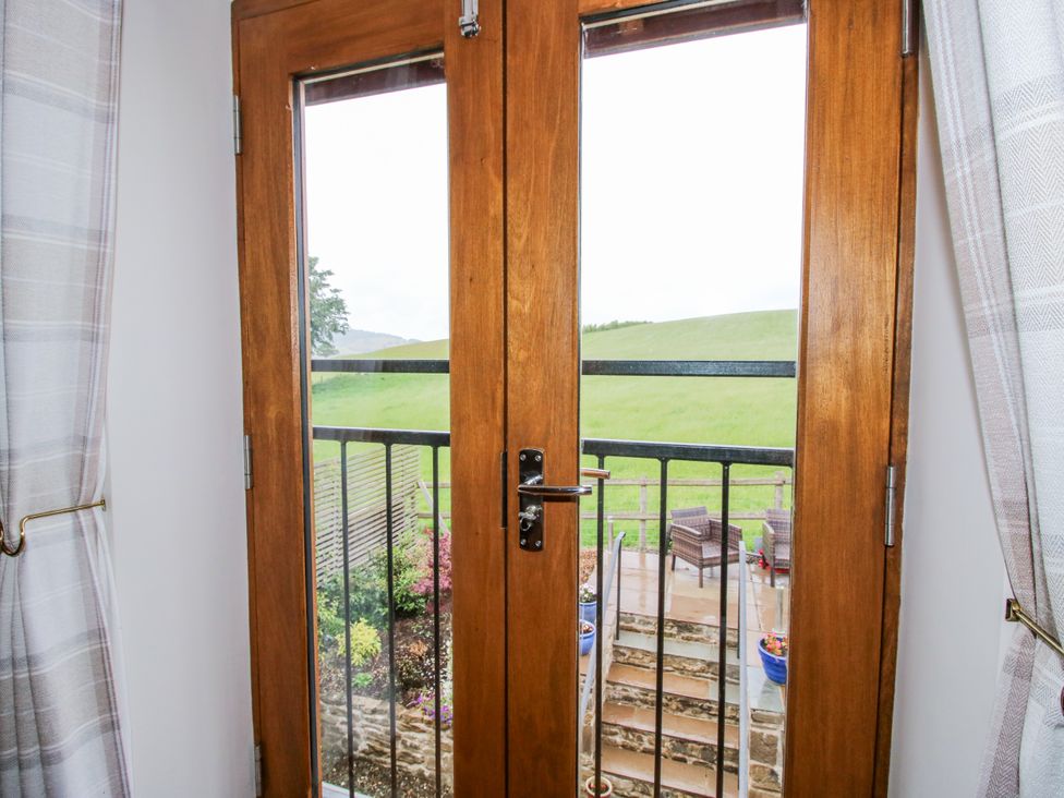 A view from double doors onto a balcony with steps at Meadow Barn in Aston On Clun