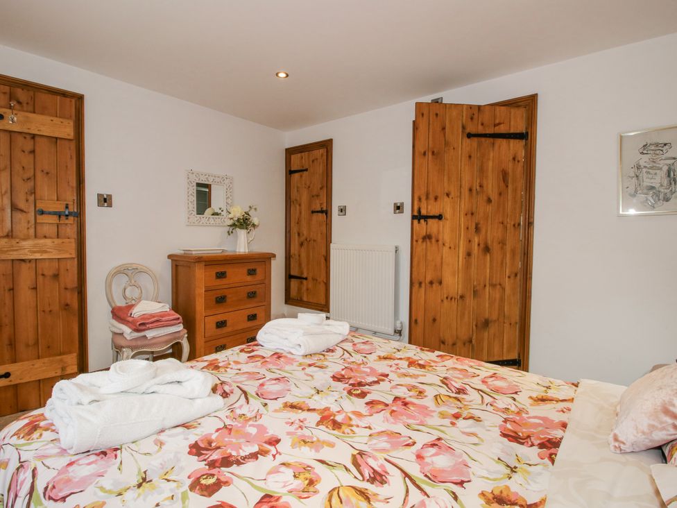A bedroom with floral bedspread and wooden furniture at Meadow Barn in Aston On Clun