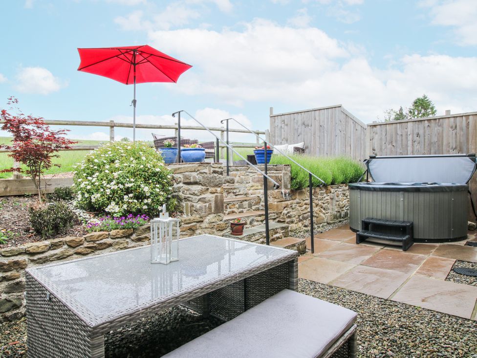 A garden with a hot tub, table, and umbrella at Meadow Barn in Aston On Clun