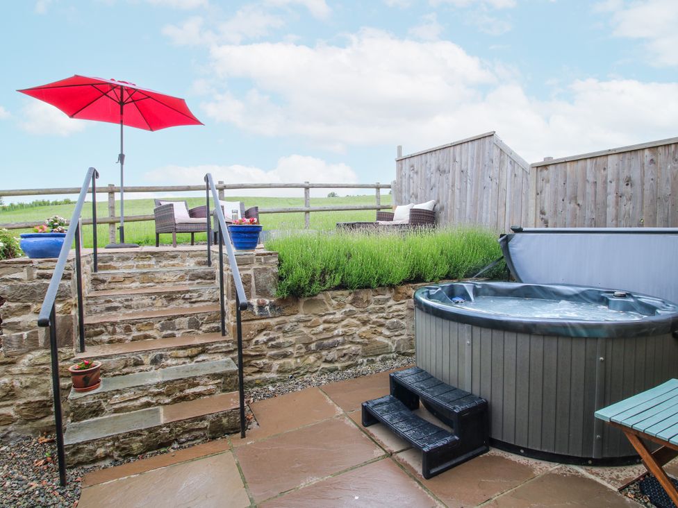 An outdoor area with a hot tub and seating at Meadow Barn in Aston On Clun