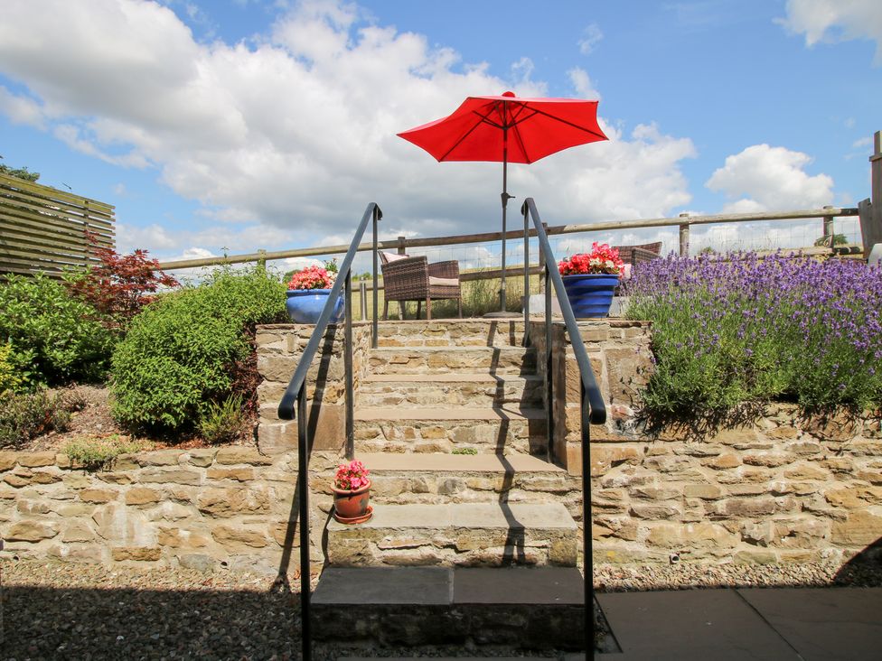 A garden with stairs leading to a chair and red umbrella at Meadow Barn Aston On Clun