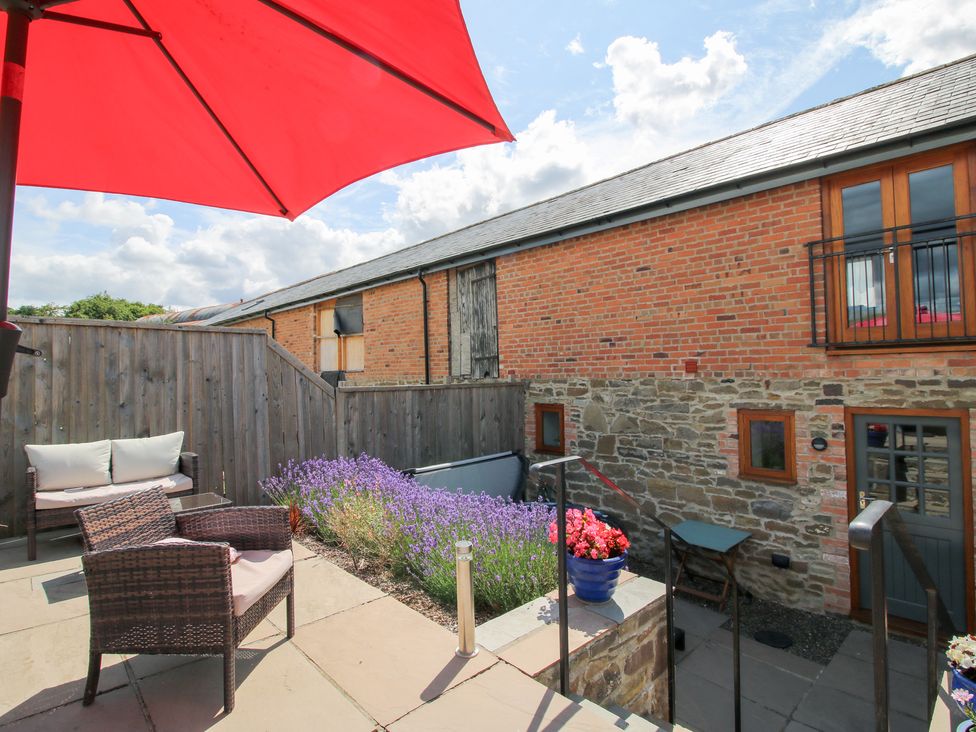 An outdoor patio area with a sofa under a red umbrella at Meadow Barn Aston On Clun