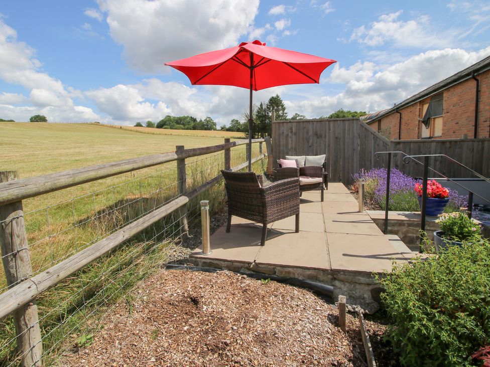 An outdoor terrace with chairs and an umbrella at Meadow Barn in Aston On Clun