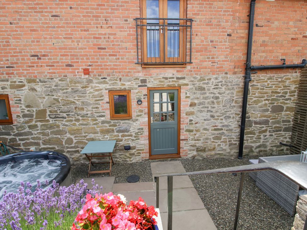 An outdoor area featuring a hot tub, table, and flowers at Meadow Barn Aston On Clun