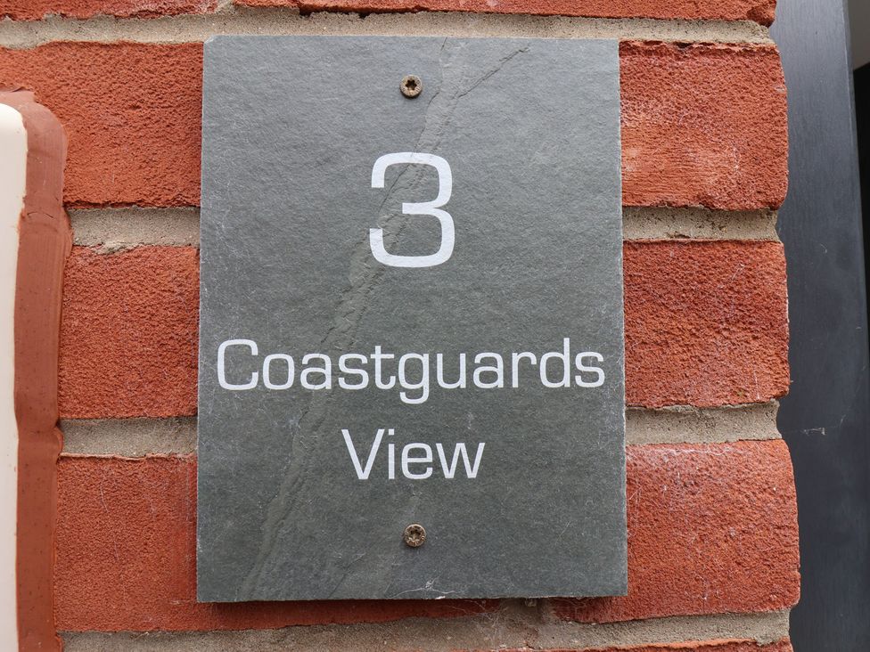 A gray plaque with the number 3 and the words Coastguards View mounted on a red brick wall at Coastguards View Whitby