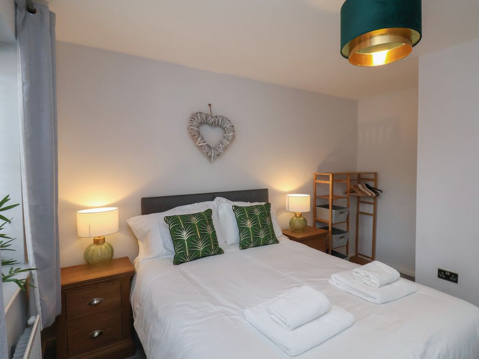 A bedroom with a double bed two bedside tables with lamps a wooden shelf unit and heart wall decor at Coastguards View in Whitby