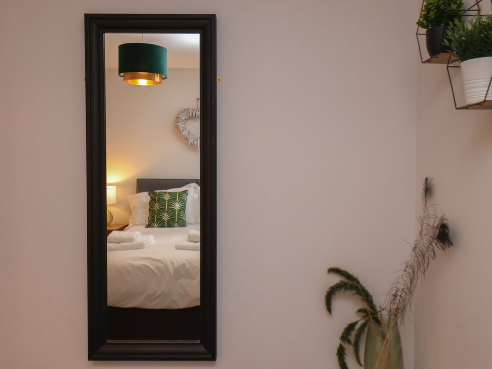 A bedroom reflected in a mirror with a bed a lamp on a nightstand and wall decorations at Coastguards View Whitby