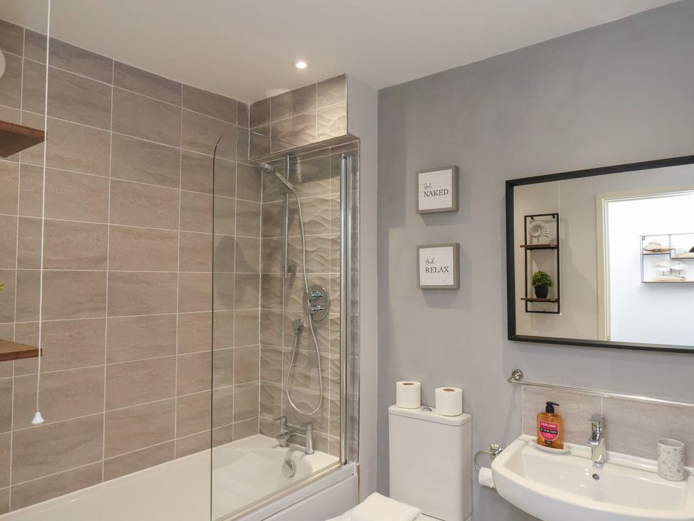 A bathroom with a bathtub shower combination sink toilet and mirror at Coastguards View Whitby