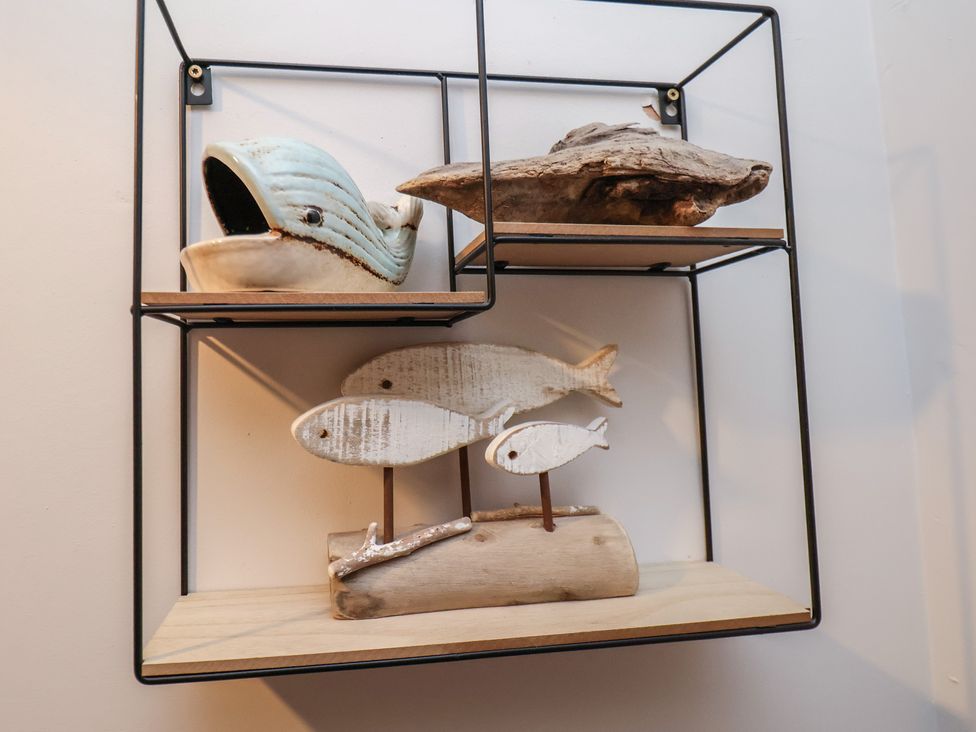 A black metal wall shelf with wooden surfaces holding a ceramic whale, a driftwood piece, and three white wooden fish on stands