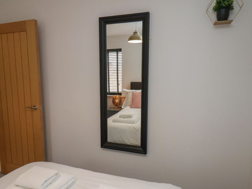 A bedroom with a wooden door a hanging mirror a bed with folded towels and reflected window and bedside lamp at Coastguards View Whitby