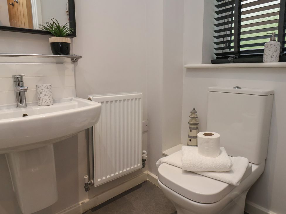 A bathroom with a white sink, radiator, toilet with towels and toilet paper, a small lighthouse decoration, plants on a shelf and window blinds at Coastguards View in Whitby