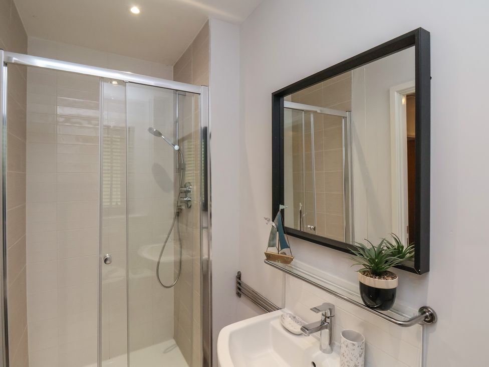 A bathroom with a glass shower enclosure a sink wall mirror and a potted plant at Coastguards View Whitby