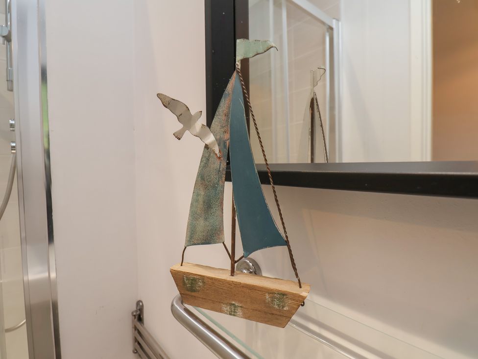 A metal and wood sailboat decoration hanging on a glass shelf bracket in a bathroom at Coastguards View in Whitby