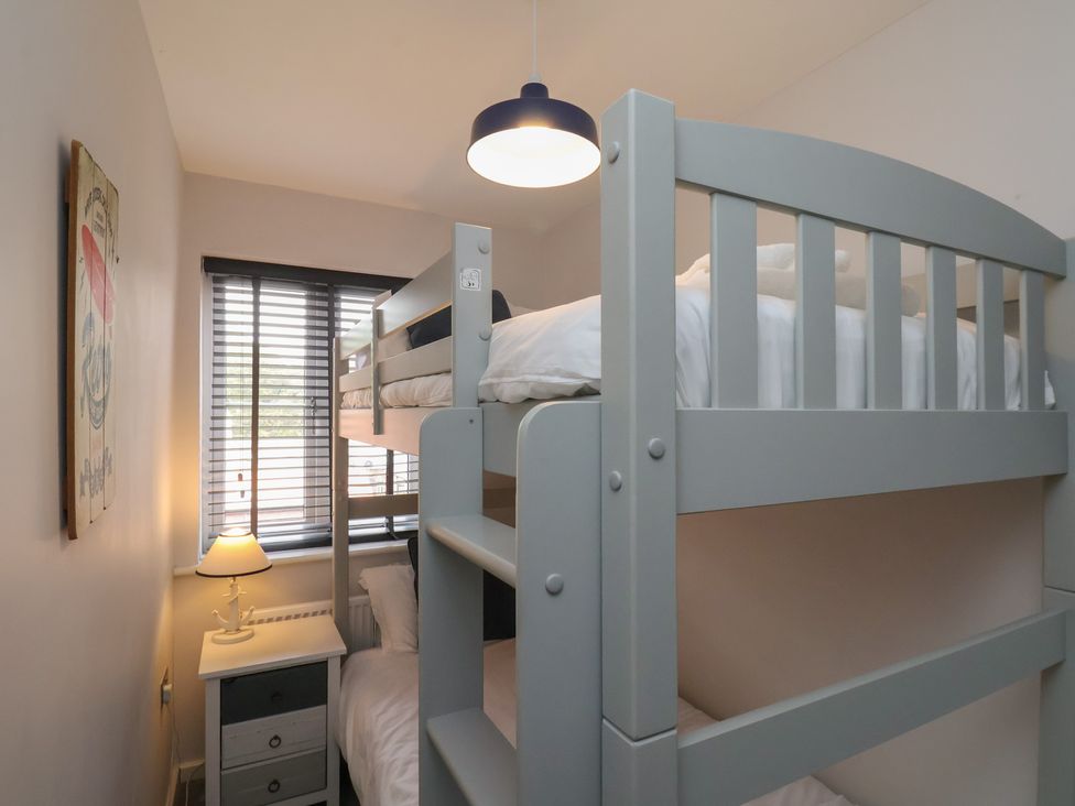 A small bedroom with a grey bunk bed a bedside table with a lamp and a window with blinds at Coastguards View in Whitby