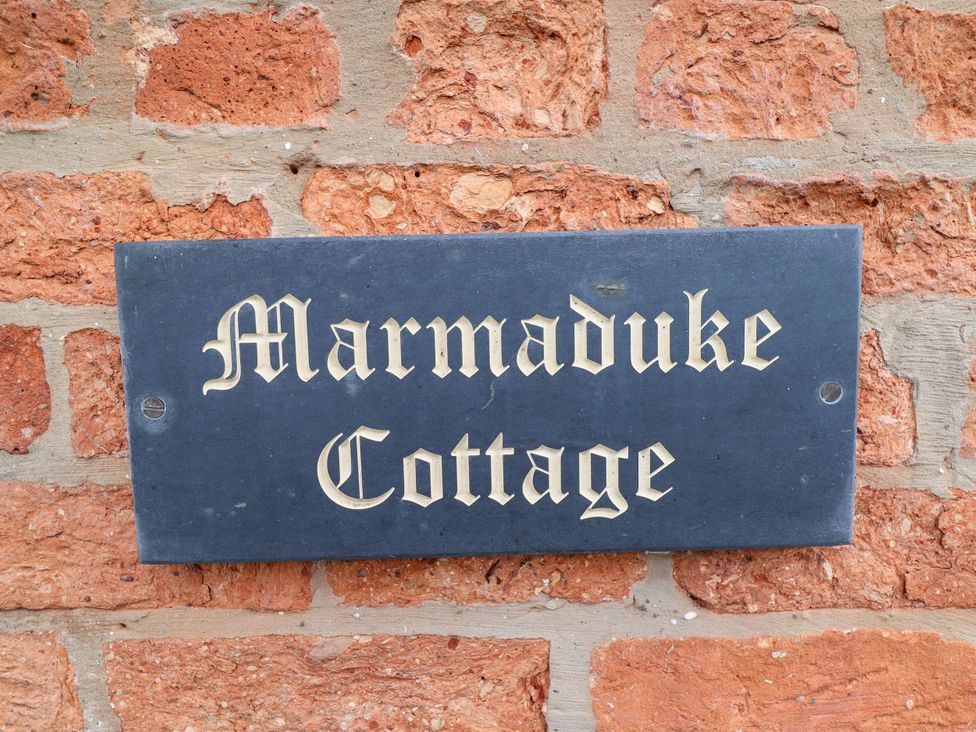 A sign that reads Marmaduke Cottage on a brick wall