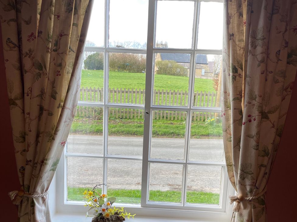 A window with curtains and a flower vase at Marmaduke Cottage in Market Weighton