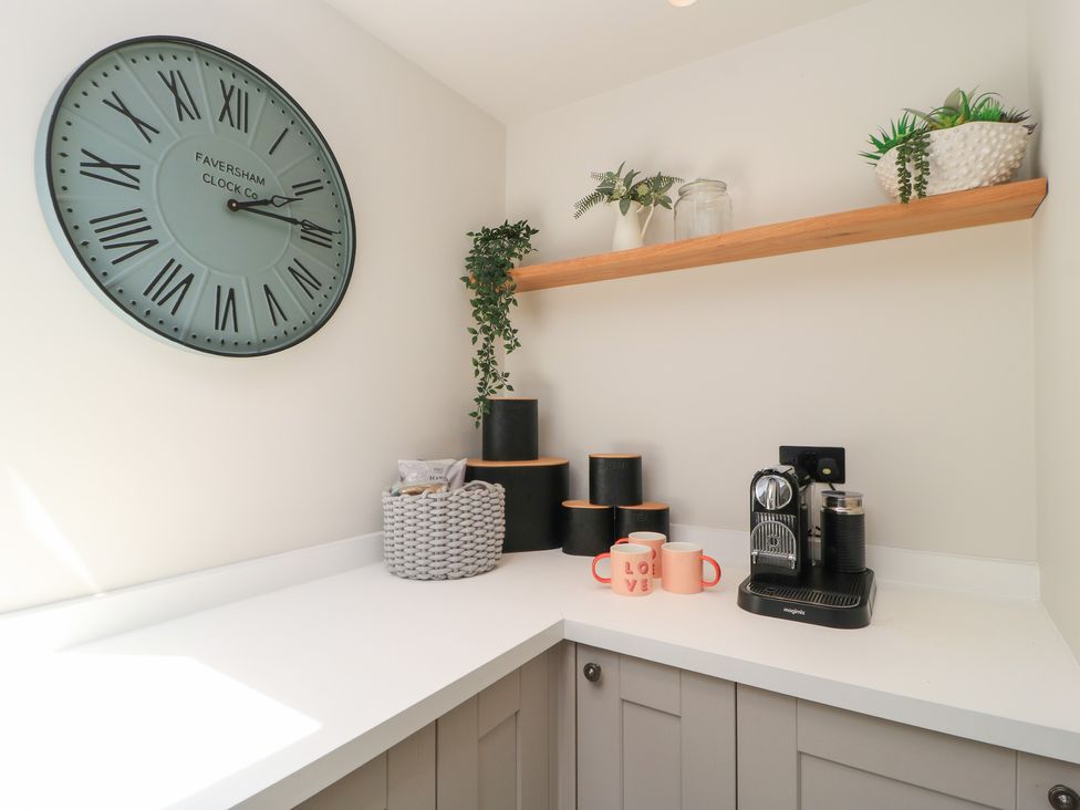 A kitchen corner with clock, shelf, coffee machine, and mugs at 12 Manor Farm Close Kingham