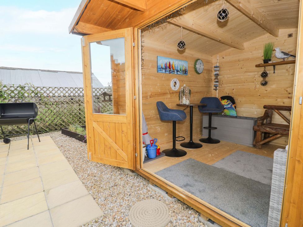 A wooden garden room with chairs and table at Cae Berllan in Mynytho near Pwllheli