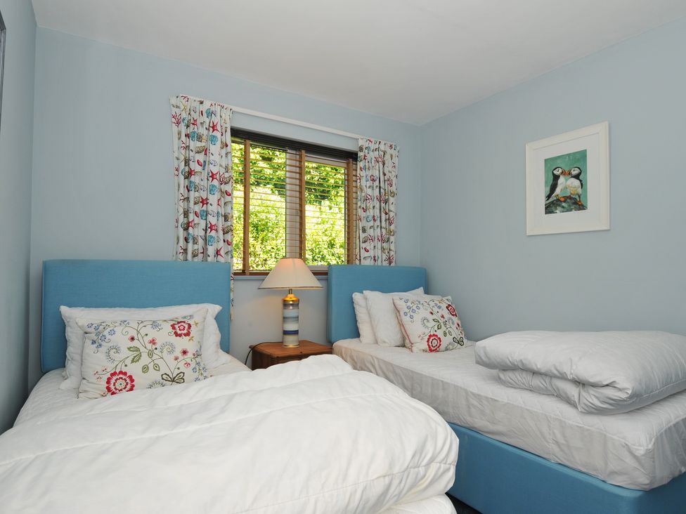 A bedroom with two single beds a window with patterned curtains and a nightstand with a lamp at Slipway 16 in Rock