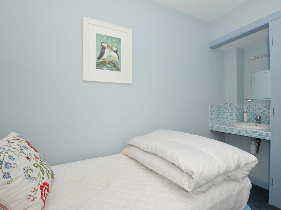 A small bedroom with a single bed and a white quilt and pillow next to a blue tiled sink with a mirror and a framed picture of two puffins on the wall at Slipway 16 in Rock