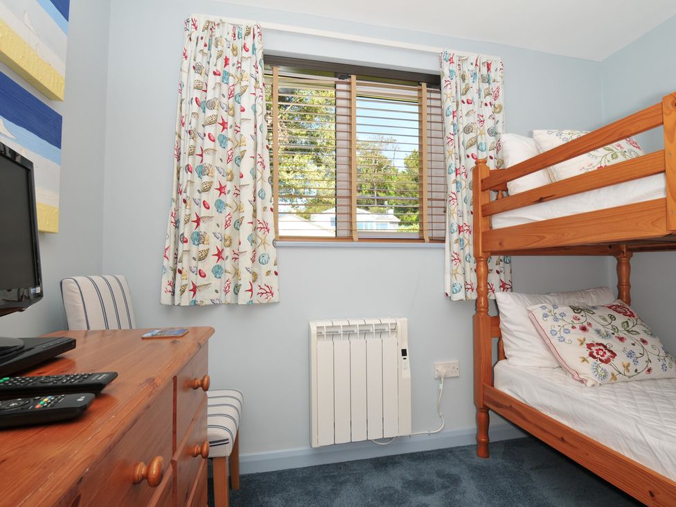 A bedroom with a bunk bed curtains with shell patterns a wooden dresser and a chair at Slipway 16 in Rock