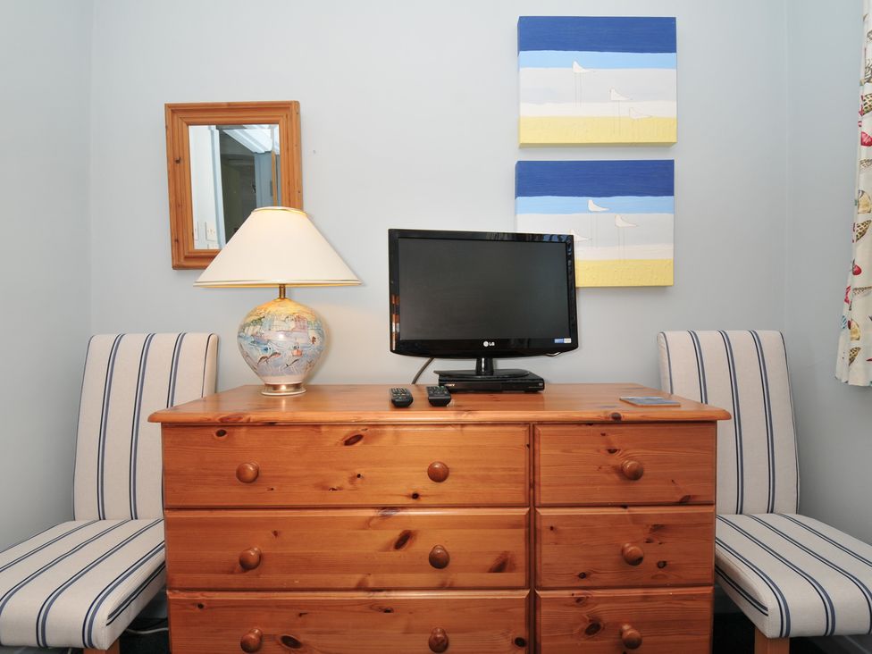 A wooden dresser with a lamp and a television flanked by two striped chairs at Slipway 16 in Rock