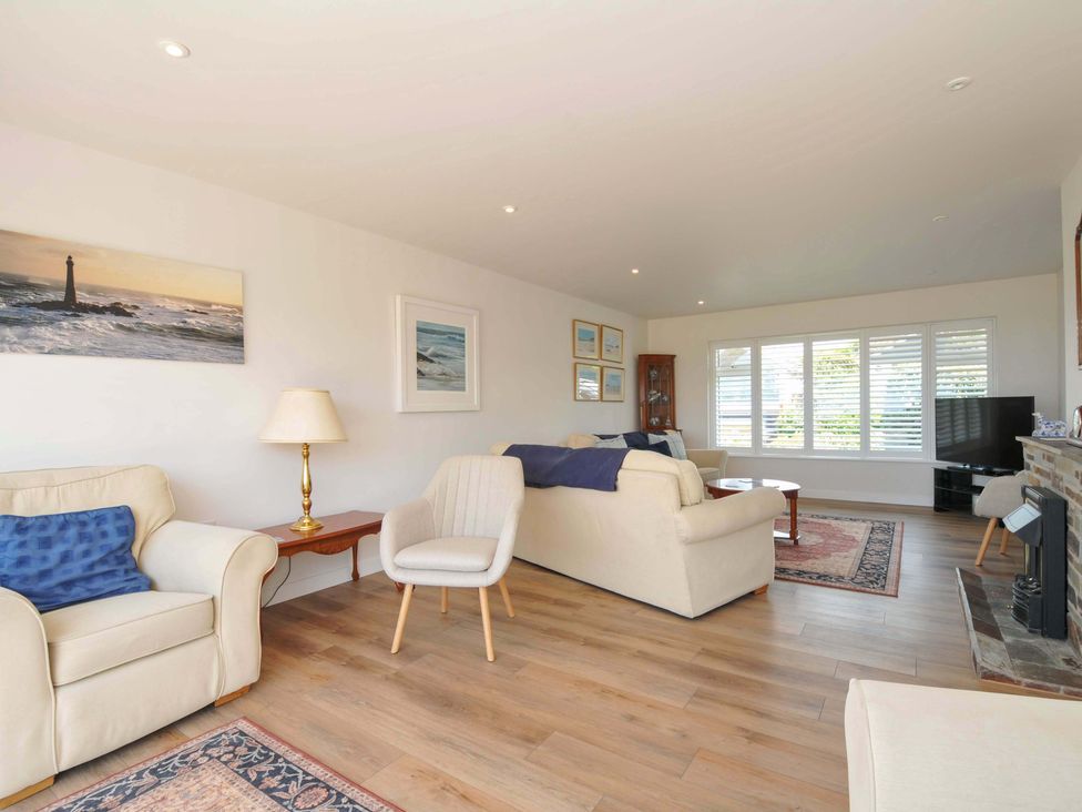 A living room with a sofa, armchair, table, and television at Sunset in Polzeath