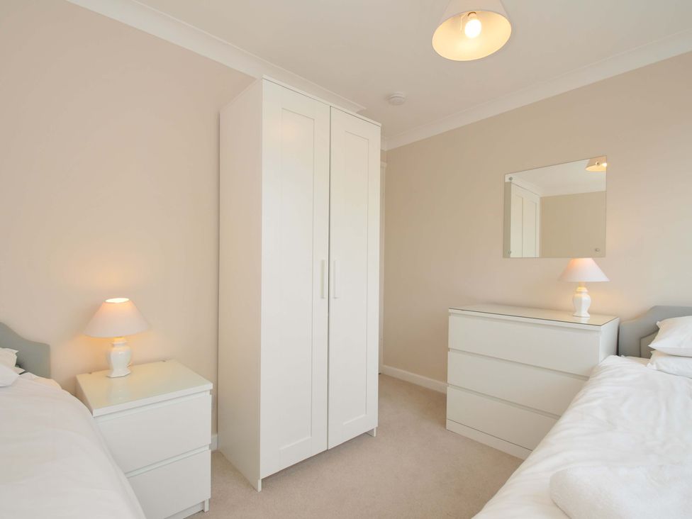 A bedroom with a wardrobe, lamp, mirror, and chest of drawers at Sunset in Polzeath