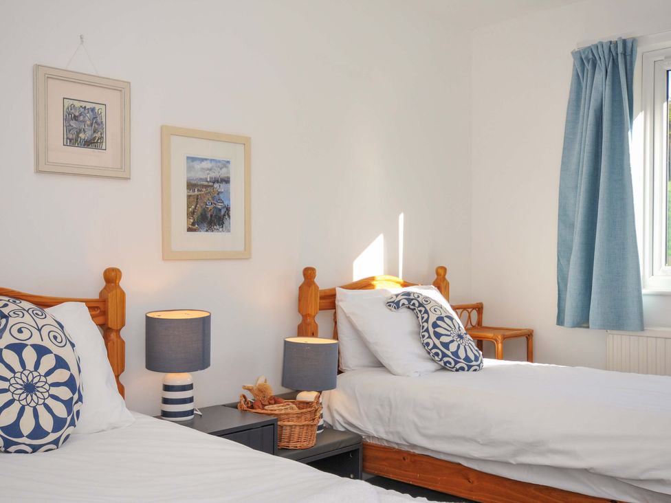 A bedroom with two beds, lamps, and artwork at Upper Gren in Trebetherick