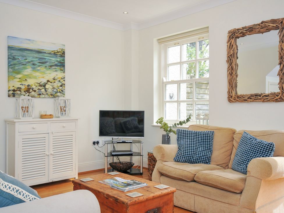 A living room with a beige sofa and blue cushions a wooden chest coffee table a white cabinet with artwork above and a television on a stand by the window at Lowenna Manor 3 in Rock