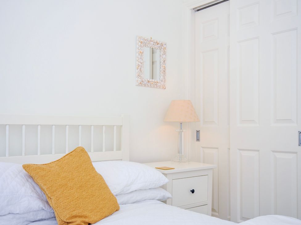 A bedroom with a white bed with a yellow pillow a white nightstand with a lamp and a small mirror on the wall at Lowenna Manor 3 in Rock