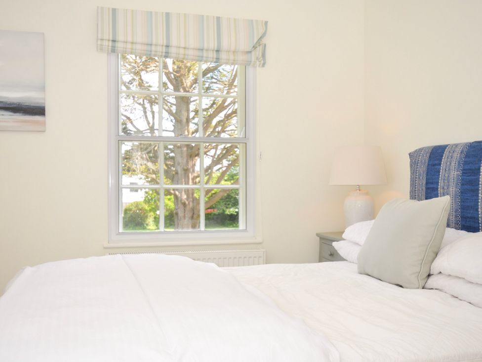 A bedroom with a white bed and a blue headboard next to a window with a tree outside at Lowenna Manor 3 in Rock