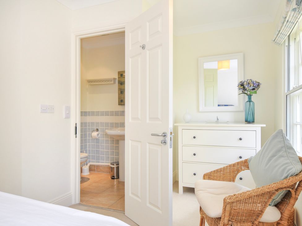 A bedroom with a wicker chair, white chest of drawers, mirror, and an open door to a bathroom at Lowenna Manor 3 in Rock