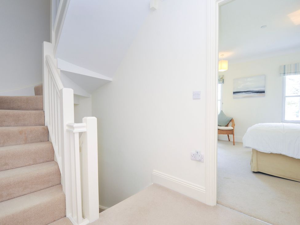 A carpeted staircase leading to a hallway with an open door to a bedroom with a bed a wicker chair and wall art at Lowenna Manor 3 in Rock